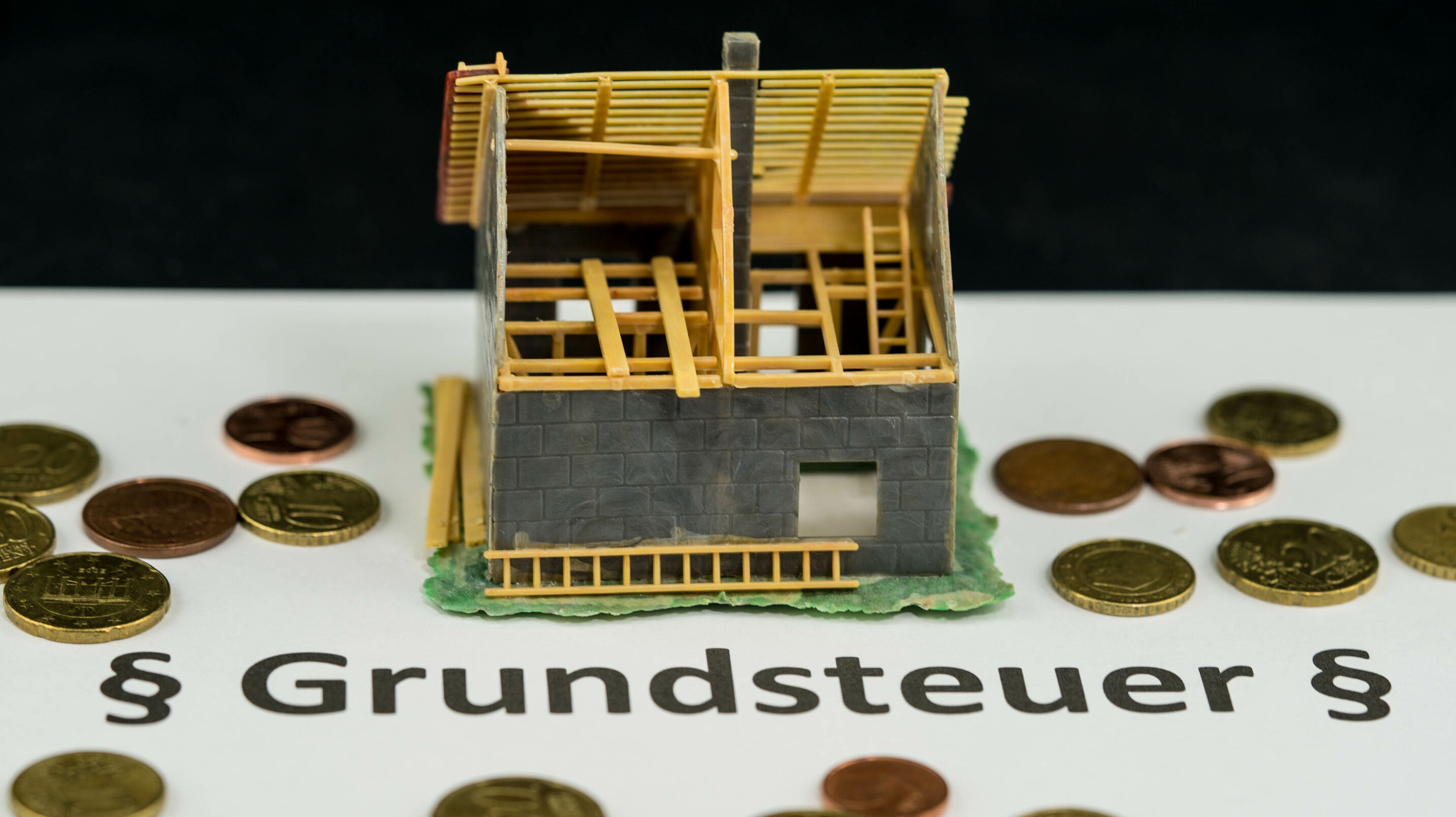Modell eines Hauses mit Geldstücken drumherum und dem Schriftzug Grundsteuer