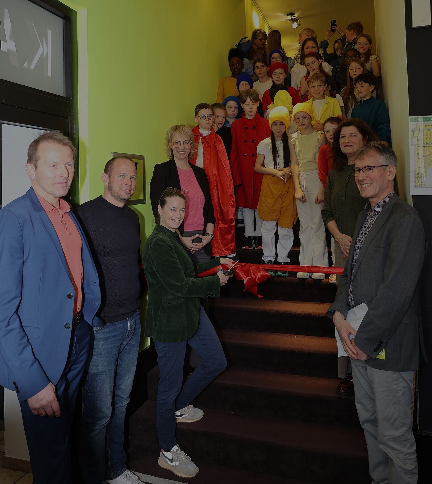 Viele Kinder auf einer Treppe. Davor stehen Erwachsene.