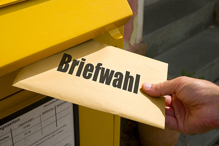 Briefwahl Hand wirft Umschlag mit Briefwahlunterlagen in öffentlichen Briefkasten