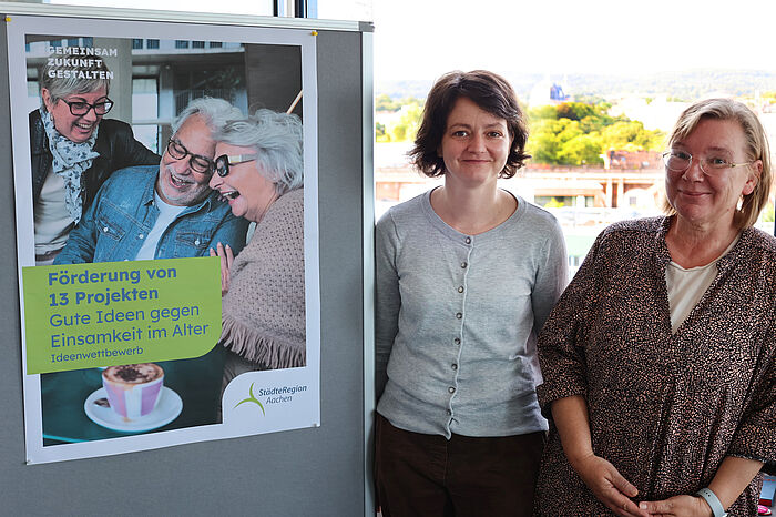 Zwei Frauen neben einem Plakat mit älteren Menschen.