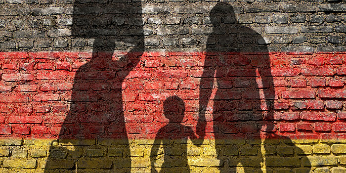 Schatten einer Familie mit Gepäck vor einer Wand in Deutschlandfarben