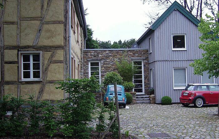 links Fachwerkhaus, mittig Anbau (mit Bruchsteinverkleidung) als Verbindungstrakt zum Anbau rechts in Form eines Holzhauses