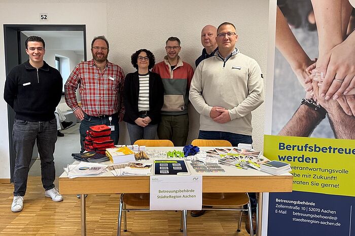 Sechs Personen hinter einem Tisch und einem Aufsteller zum Thema Berufsbetreuer_innen.