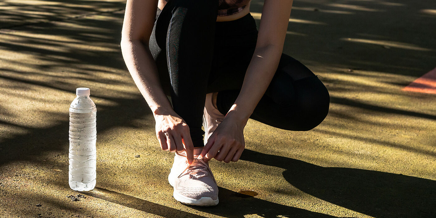 Sportler bindet Schuhe im Schatten, daneben steht eine Wasserflasche