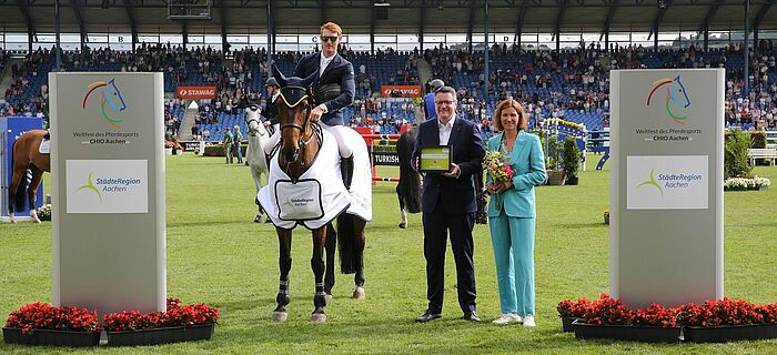 Siegerehrung: Die Präsidentin des Aachen-Laurensberger Rennvereins Stefanie Peters und Städteregionsrat Dr. Tim Grüttemeier überreichen dem glücklichen Sieger Daniel Coyle den Ehrenpreis der StädteRegion Aachen.