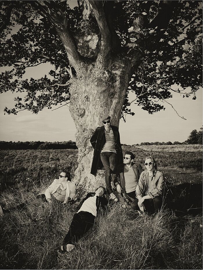 Fünf Männer liegen bzw. stehen an einem Baum