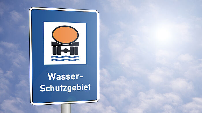 Das blaue Schild mit Wasser-Schutzgebiet vor blauem Himmel mit leichten weißen Wolken und der Sonne