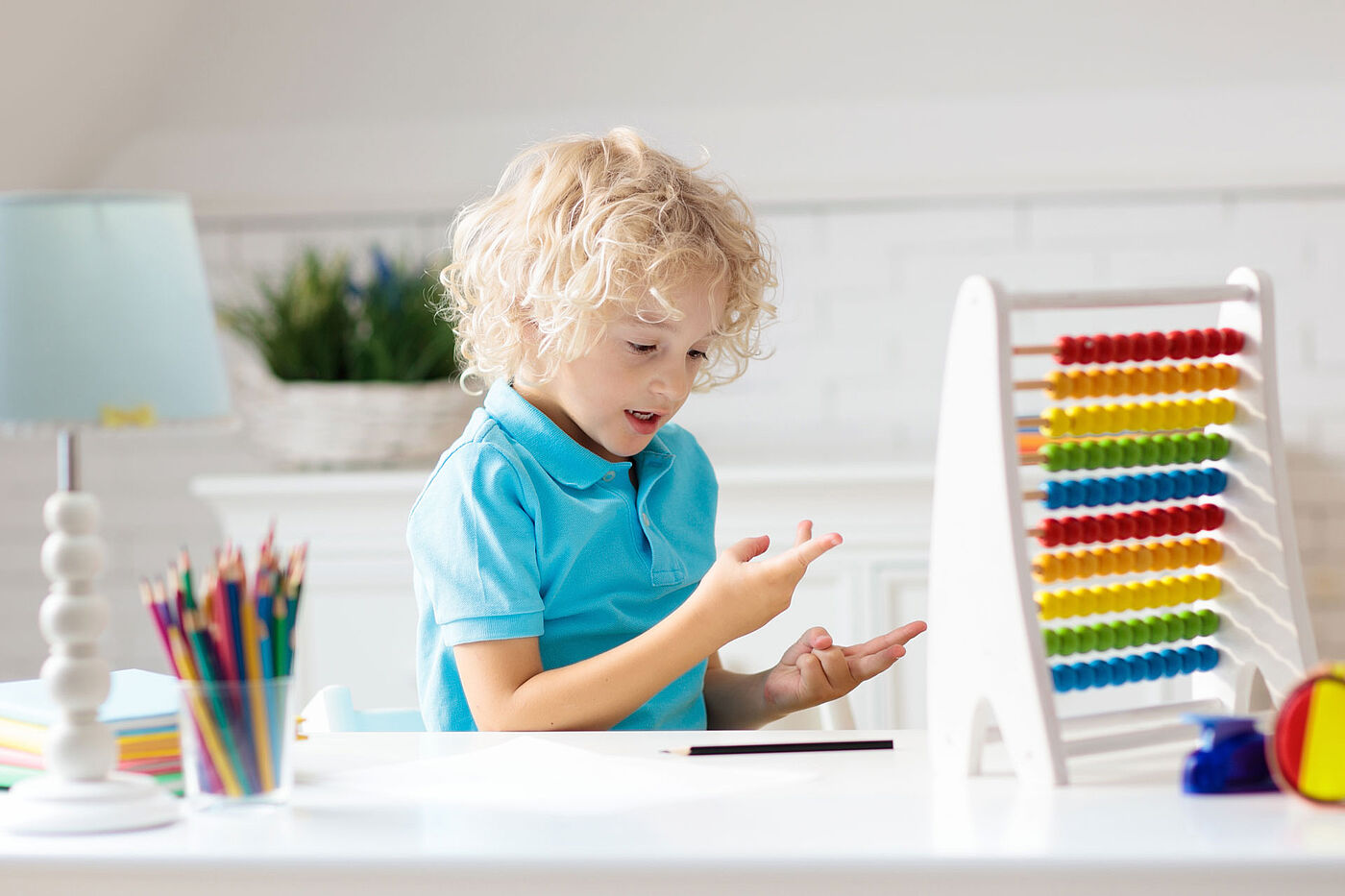 Ein Junge sitz am Schreibtisch vor einem bunten Rechenschieber und rechnet mit seinen Finger. 