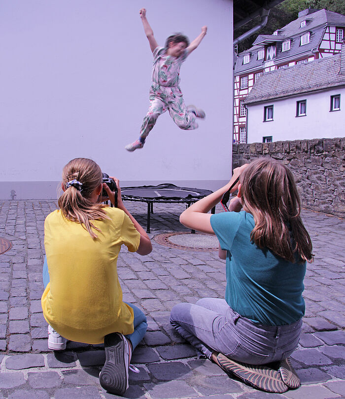 Zwei Kinder fotografieren ein Kind, das hochspringt.