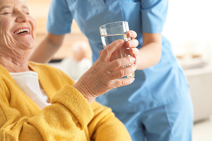 Krankenschwester gibt älterer Frau im Haus ein Glas Wasser