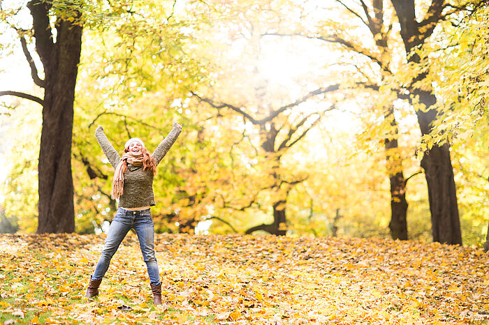 Junge Frau jubelt mit hochgerissenen Armen in herbstlicher Landschaft