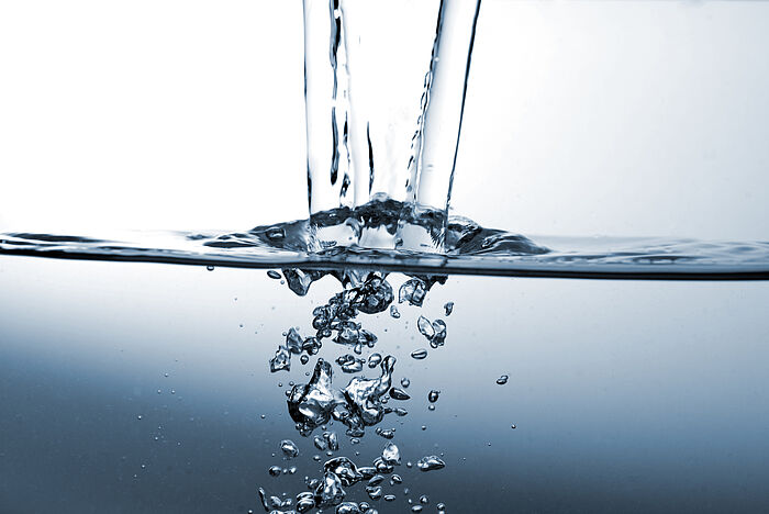 Trinkwasser Ein Wasserstrahl trifft in eine Wasseroberfläche