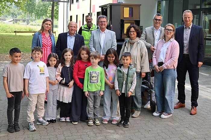 Kinder und Erwachsene vor einem Blitzer vor einer Schule.