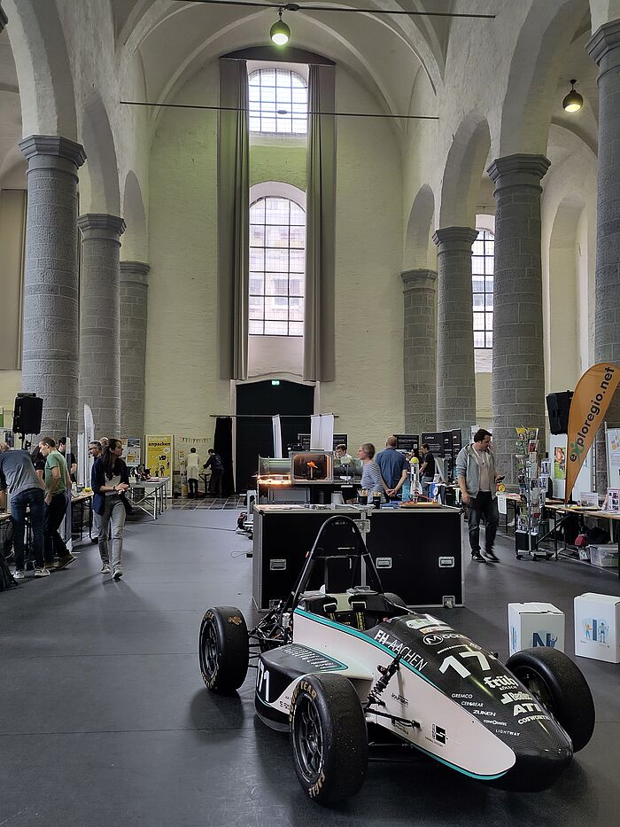Eine Aula mit Ständen und einem Auto.