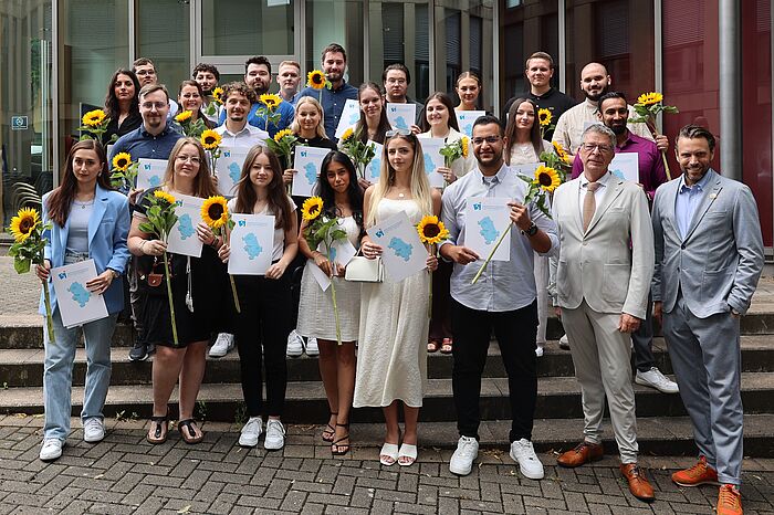Viele Menschen in schicken Anziehsachen mit Sonnenblumen in der Hand.