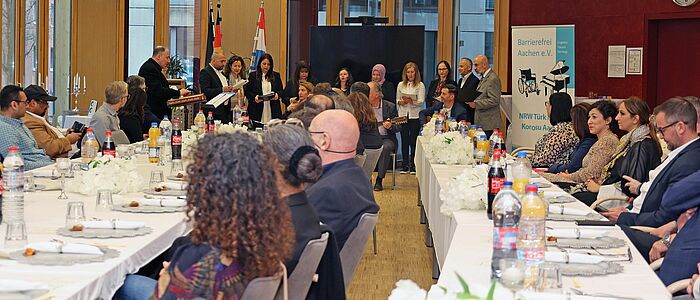 Iftar-Essen im Mediensaal der StädteRegion. Ein Chor singt, Gäste sitzen an festlich gedeckten Tischen.
