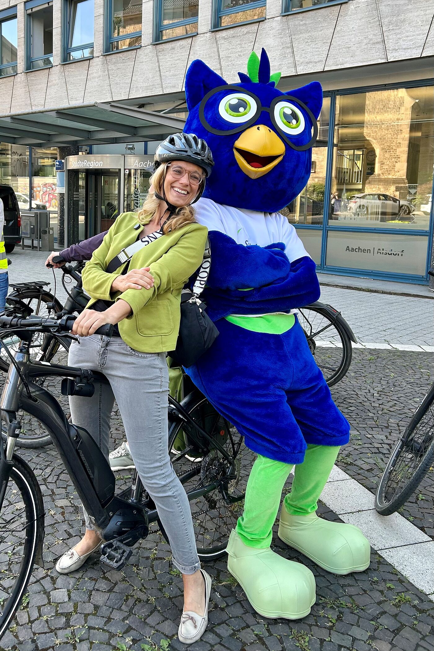 Eine Frau und eine große Plüsch-Eule auf einem Fahrrad.