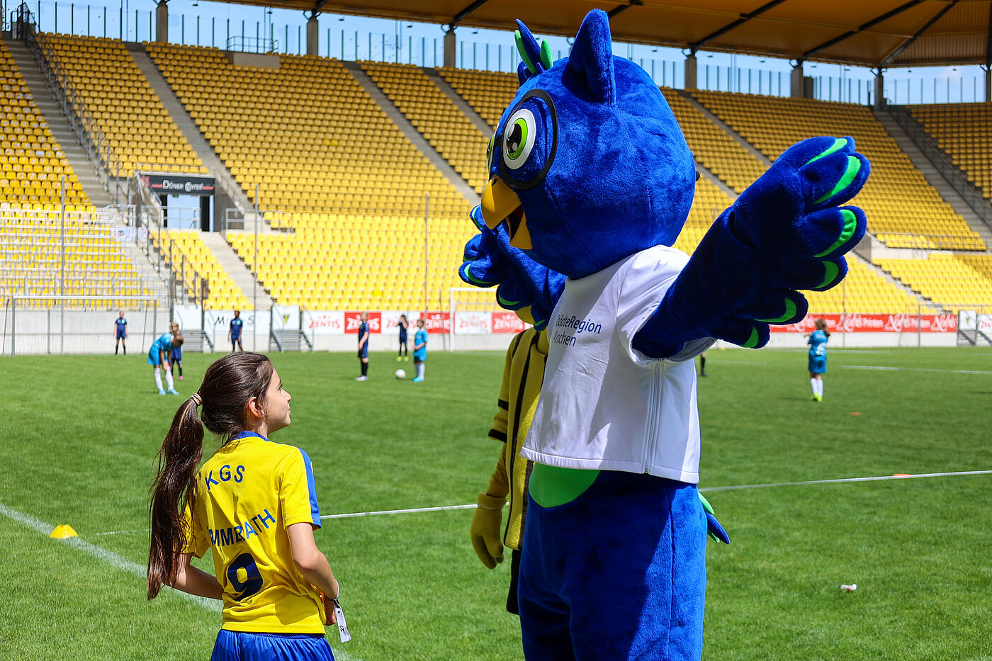 Ein Kind im Fußballtrikot mit einem Eulen-Maskottchen