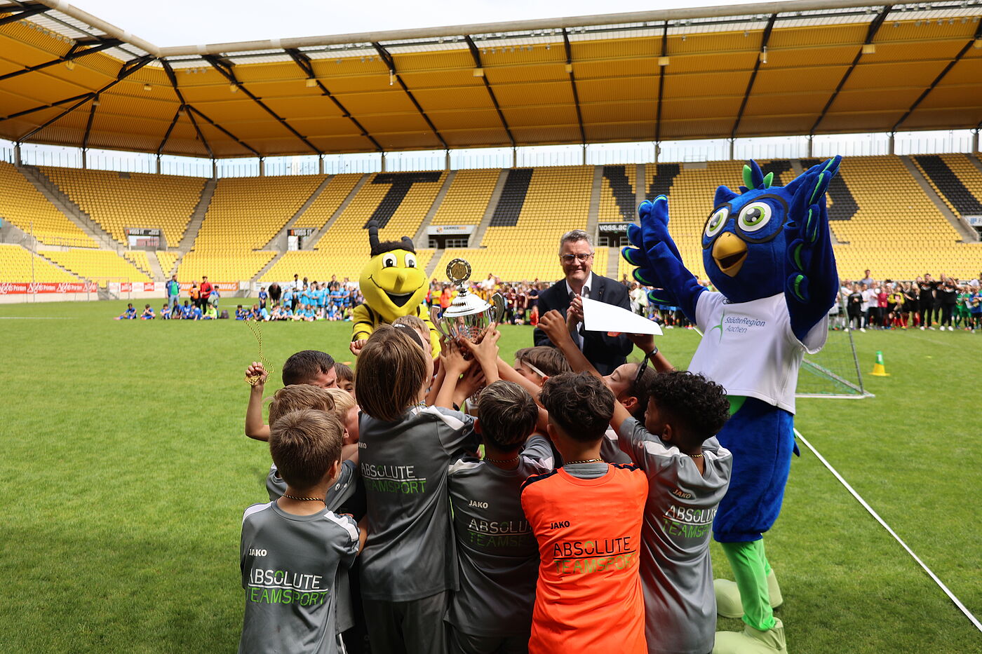 Kinder auf einem Fußballfeld mit einem Pokal und einer Stoffeule