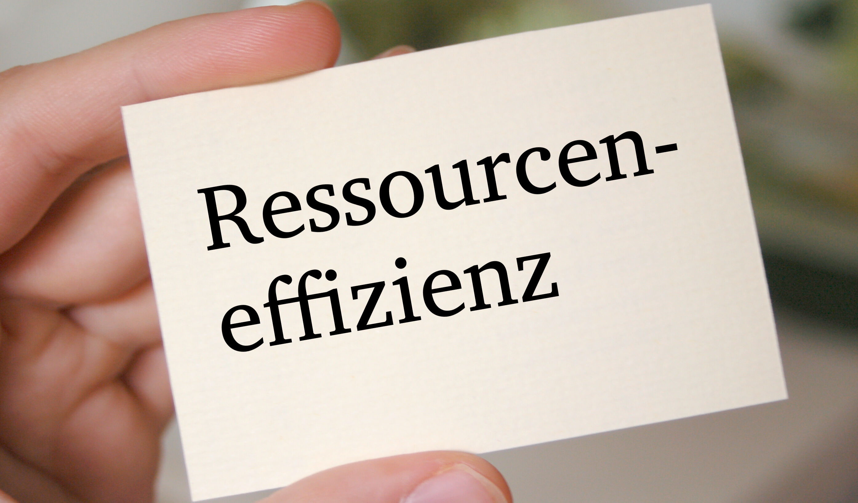 Eine Hand hält eine weiße Karte mit der Aufschrift Ressourceneffizienz fest