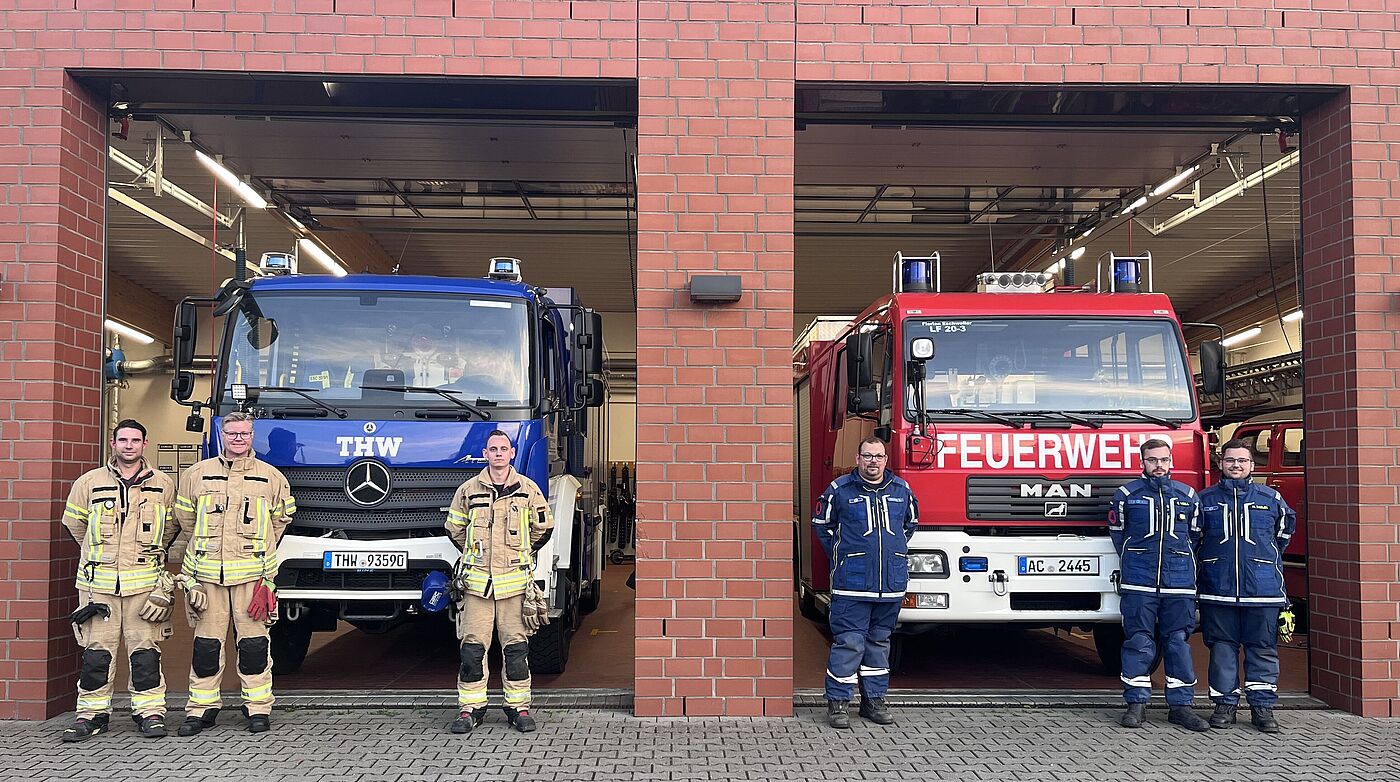 Fachkräfte von Feuerwehr und THW stehen vor deren Einsatzfahrzeugen