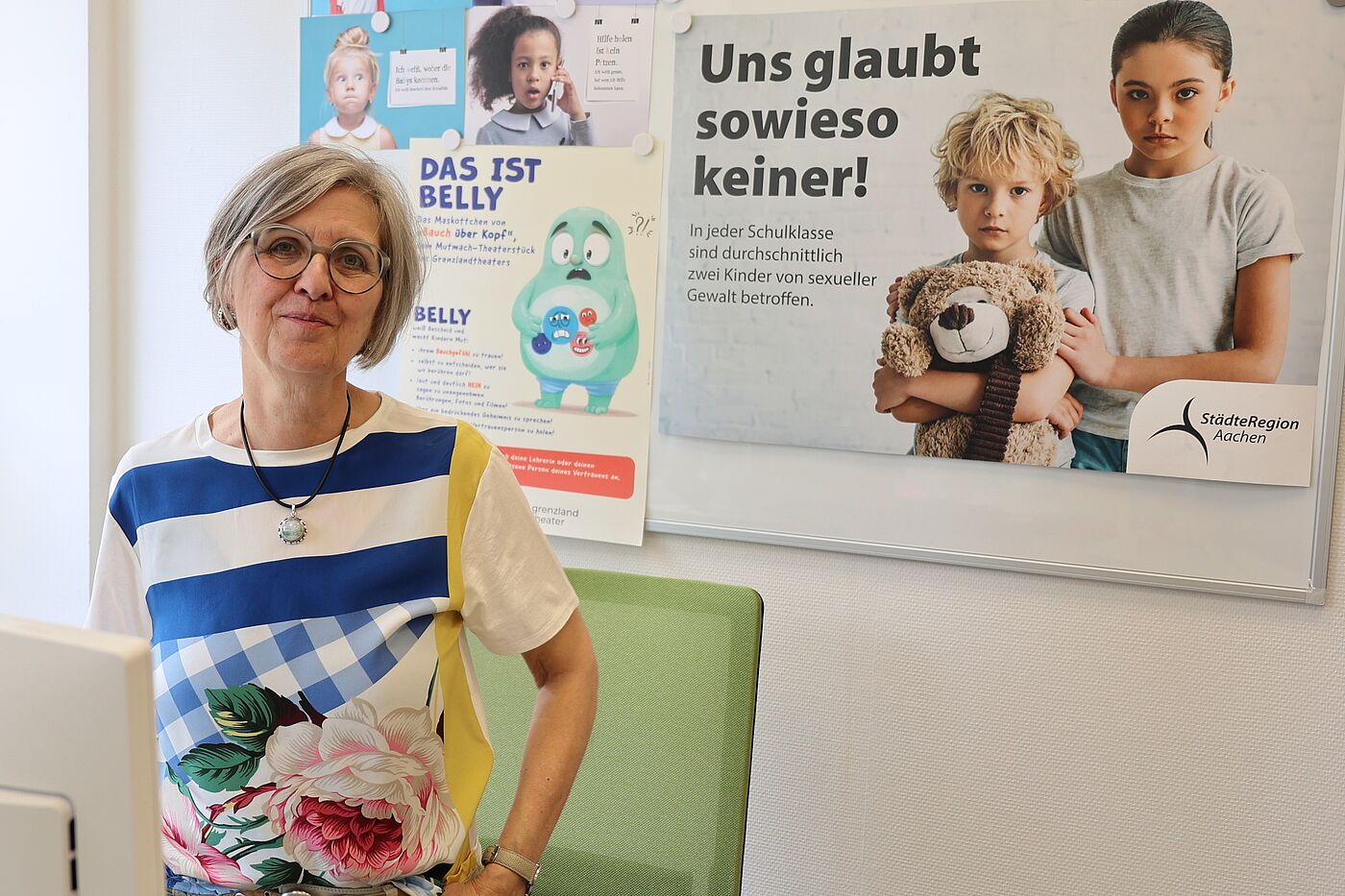 Sabine Rommel die pädagogische Leiterin der Fachstelle gegen sexuelle Gewalt an Kindern und Jugendlichen beim Amt für Kinder, Jugend und Familie der StädteRegion Aachen vor bunten Plakaten an ihrem Arbeitsplatz. 
