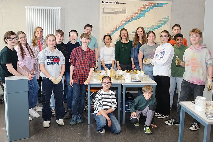 Schülerinnen und Schüler stehen in einem Klassenzimmer zusammen um einen Tisch herum. Darauf liegen Kugeln aus Blumensamen.