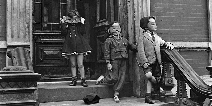Foto von Helen Levitt aus dem Howard Greenberg Archiv. Drei Kinder mit Maske auf Treppe in New York, 1940