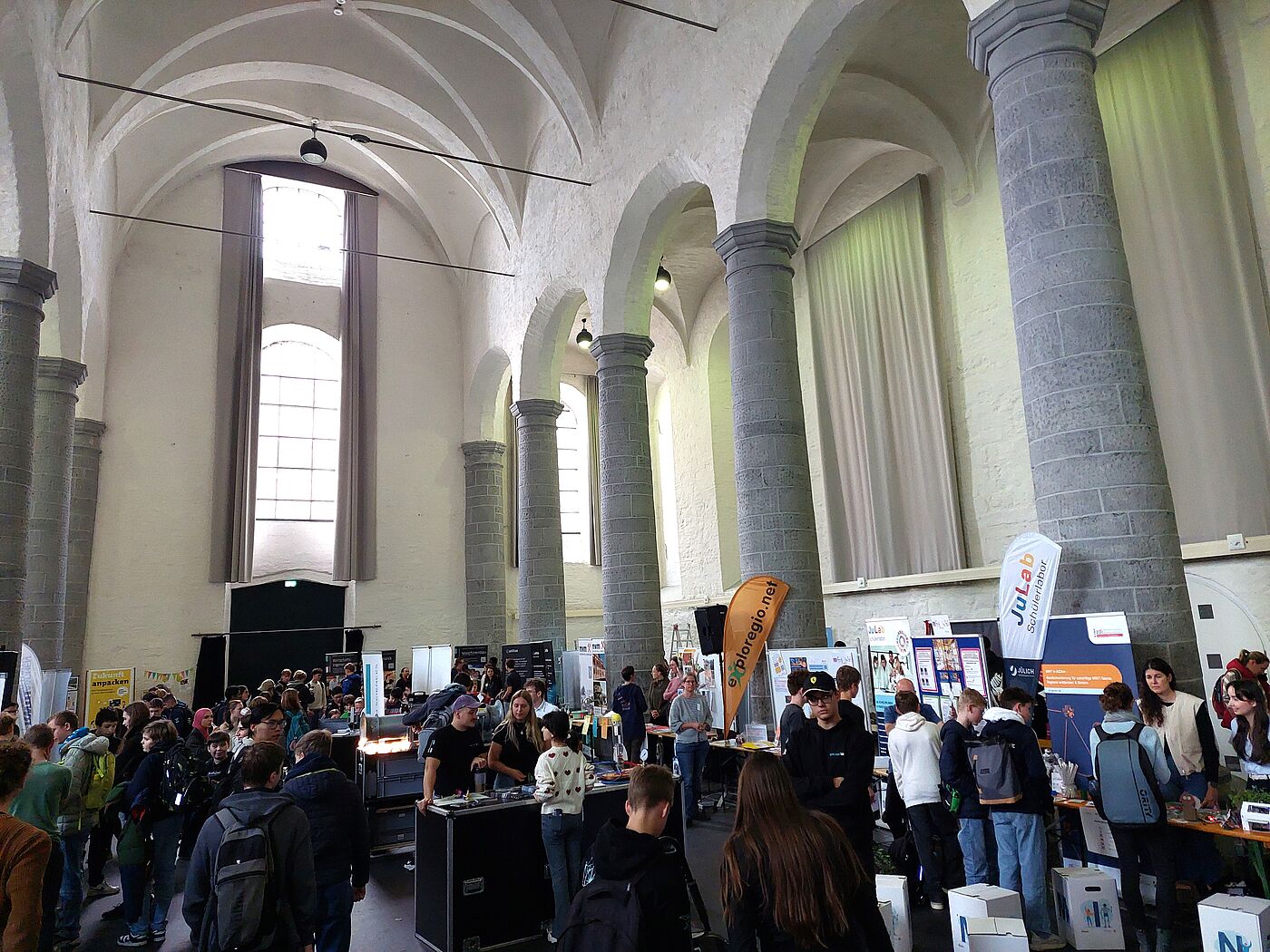 Eine Aula mit vielen Menschen an Messeständen.