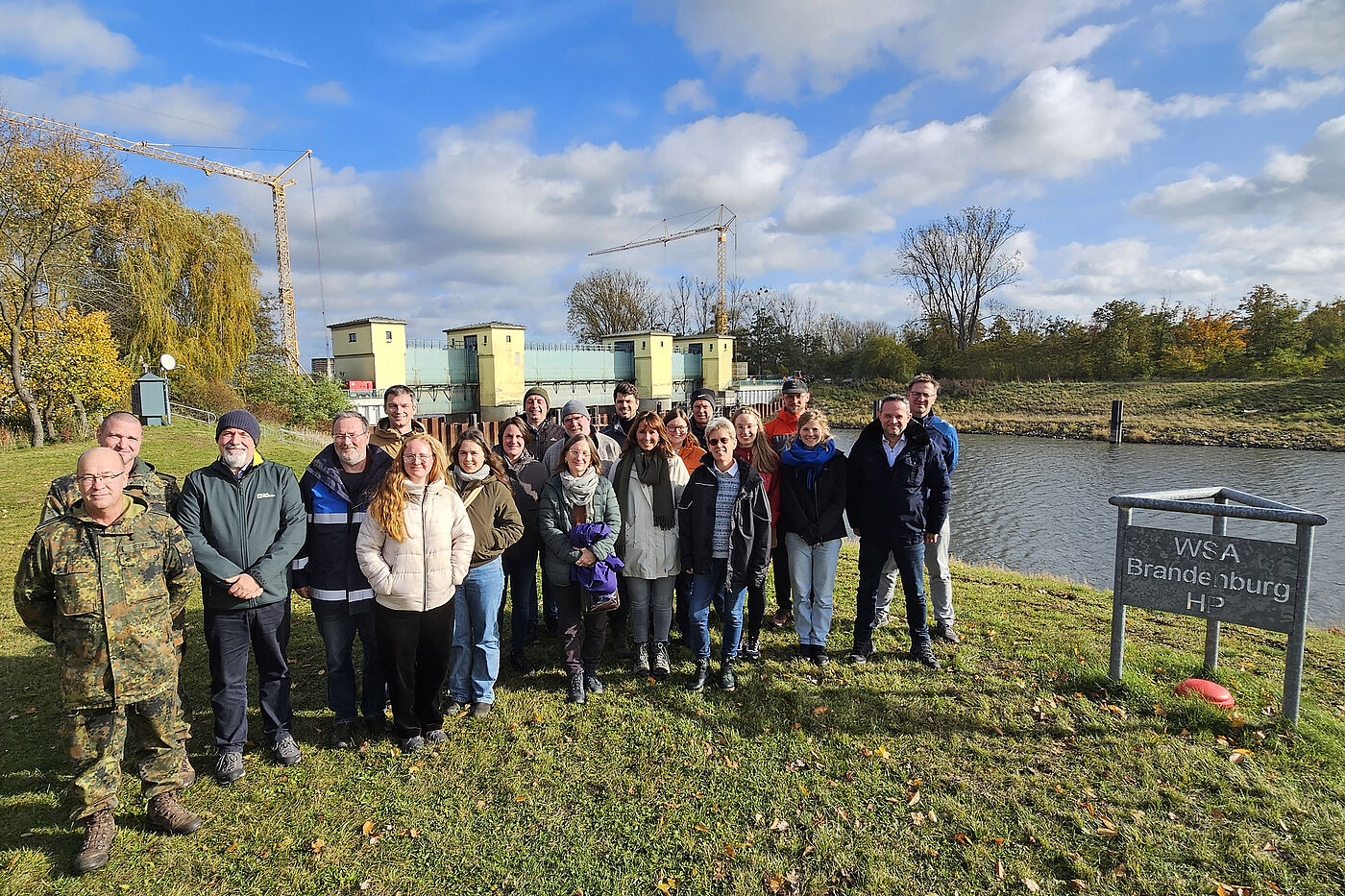 Mehrere Menschen auf einer Wiese neben einer Hochwasserschutzanlage.