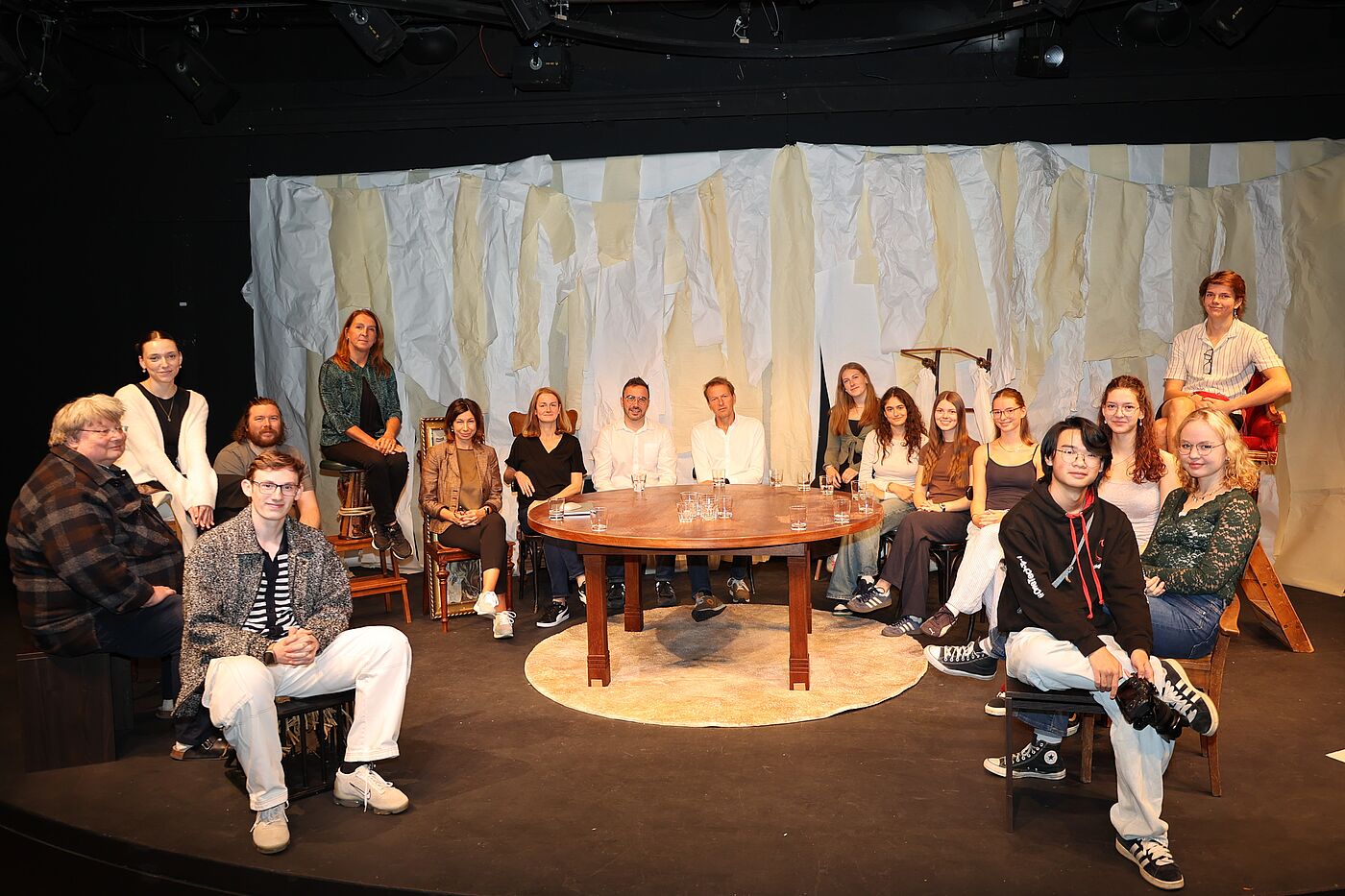 Jugendliche und Erwachsene an einem Tisch auf einer Bühne