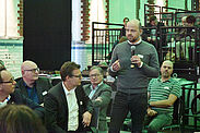Zuhörer im Saal und ein stehender Mann hält ein Mikrofon in der Hand