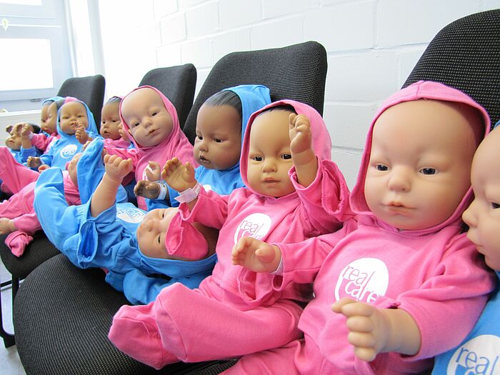 Baby Puppen sitzen aufgereiht auf Stühlen 