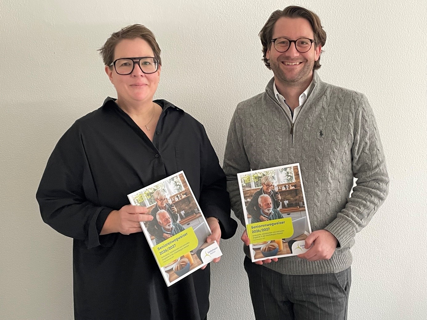 Eine Frau und ein Mann stehen nebeneinander und halten eine Broschüre in der Hand.