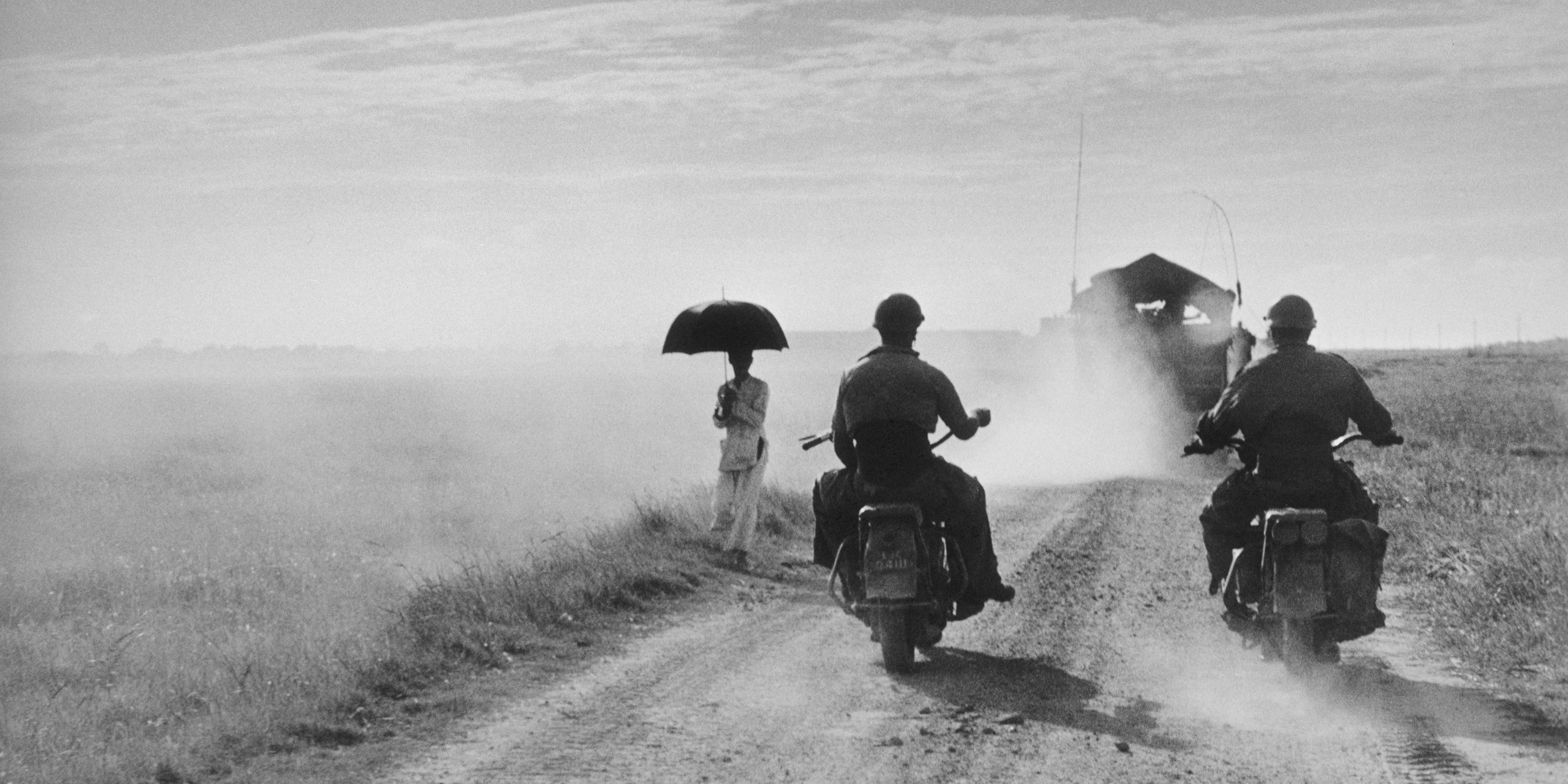Robert Capa, Motorcyclists and woman walking on the road from Nam Dinh to Thai Binh, Indochina (Vietnam), May, 1954. 
