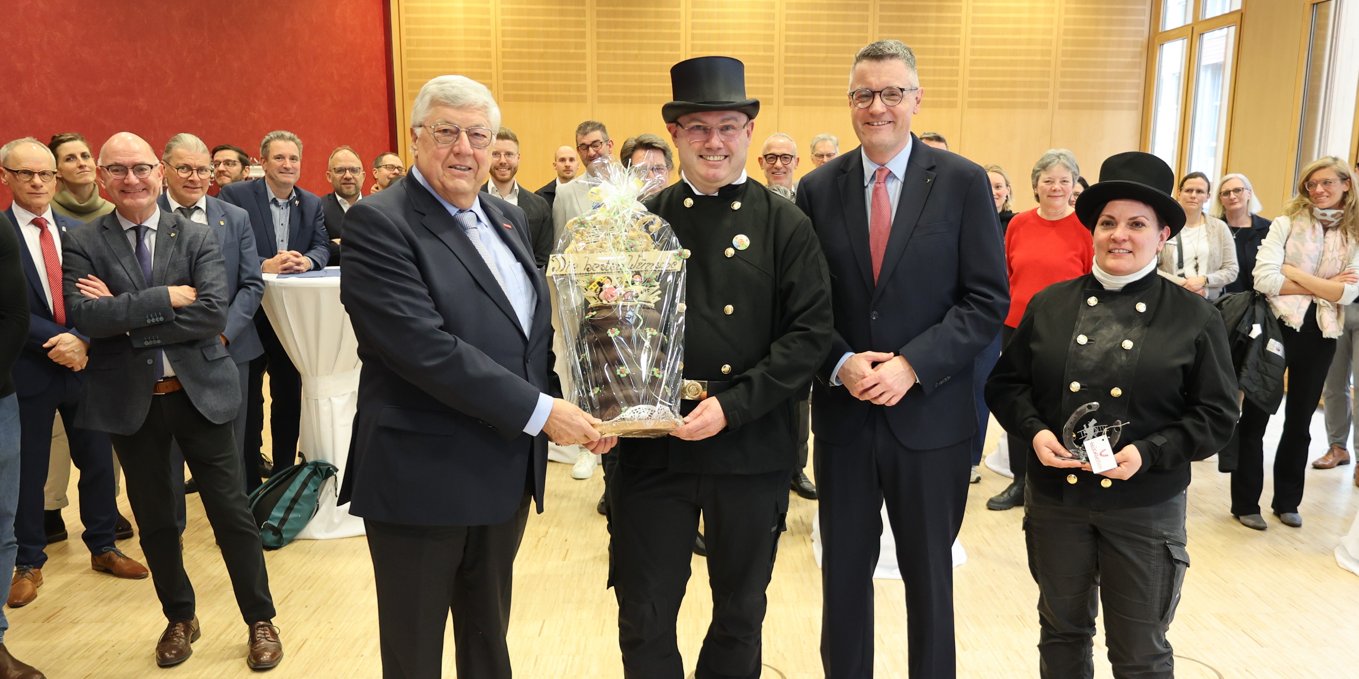 Zwei Männer, ein Schornsteinfeger und eine Schornsteinfegerin halten einen Baumkuchen