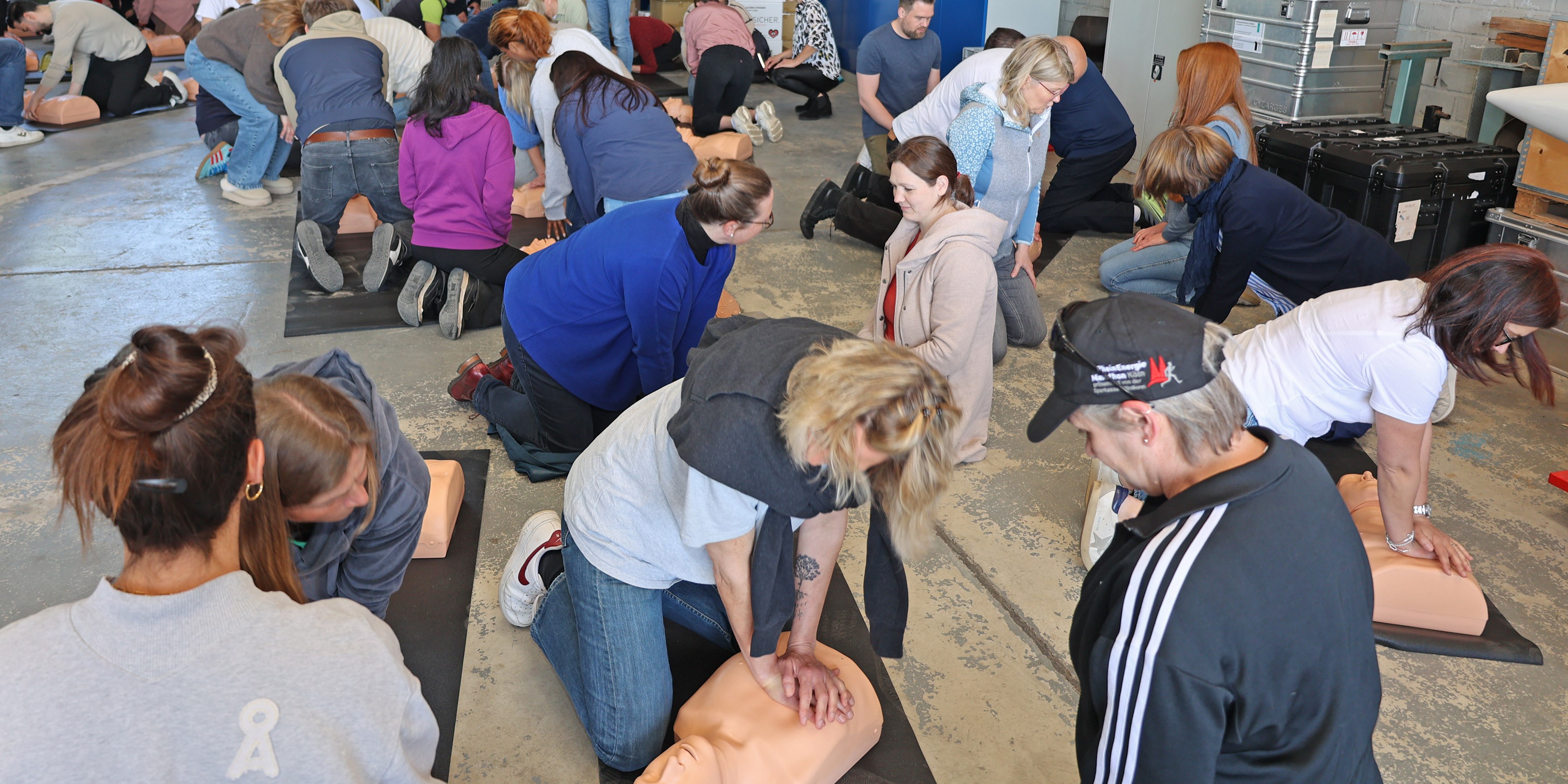 Mehrere Menschen knien auf dem Boden. Sie üben Reanimation an Puppen.