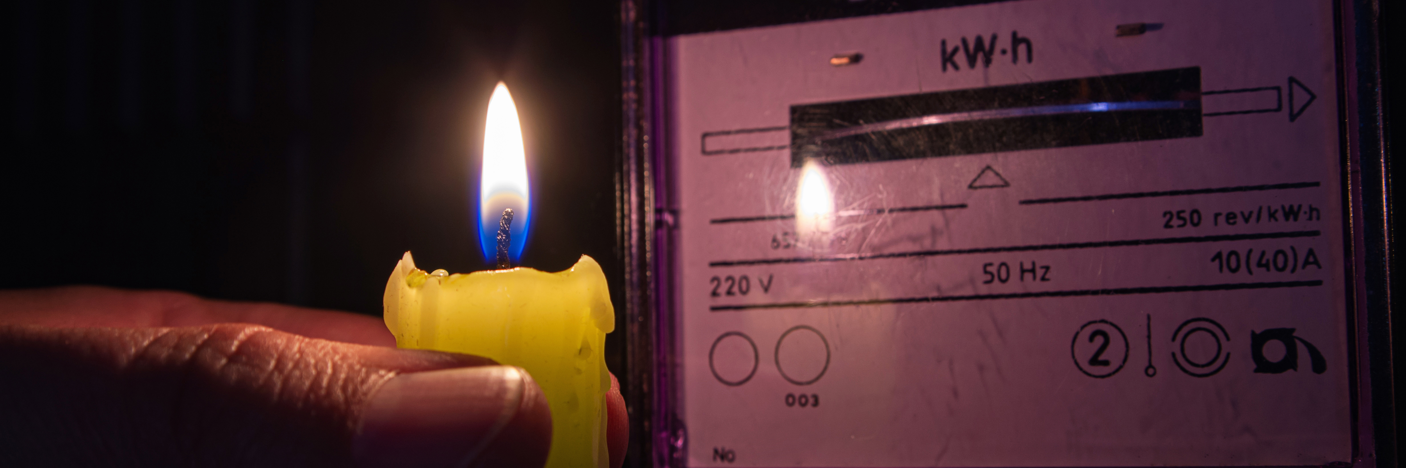 Hand mit Kerze im Dunkeln vor einem Stromzähler