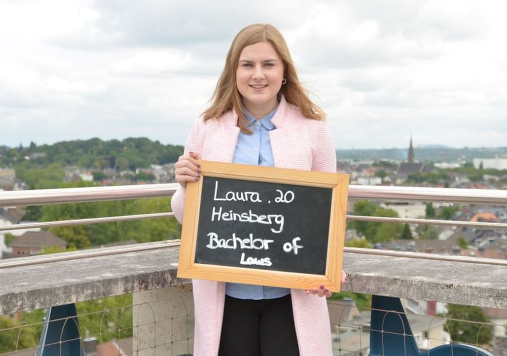 Laura hält eine Tafel mit ihrem Namen, Alter und ihrem Ausbildungsberuf