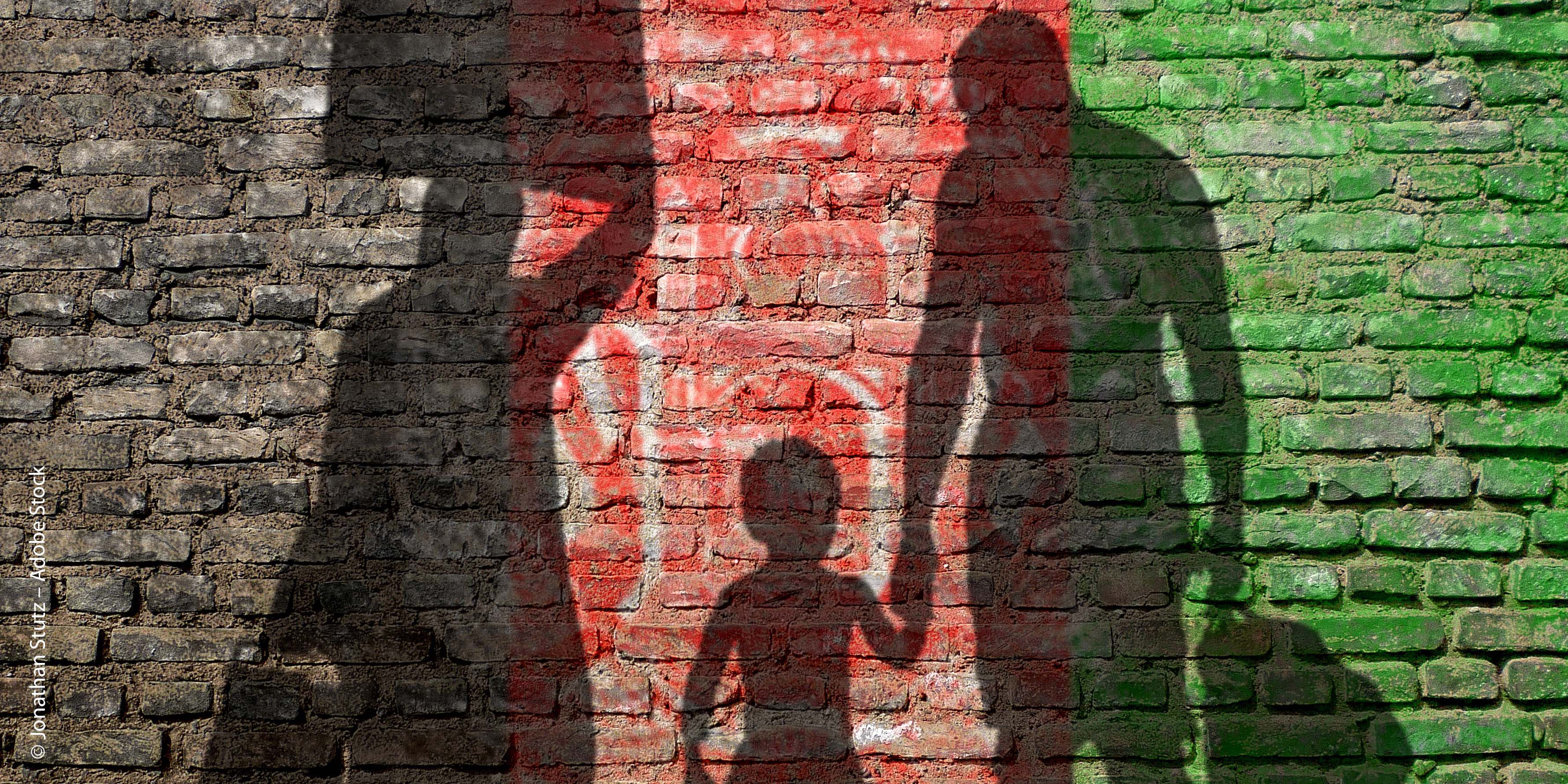 Schattenrisse von drei flüchtenden Menschen. Die Wand dahinter trägt die Farben der aghanischen Flagge