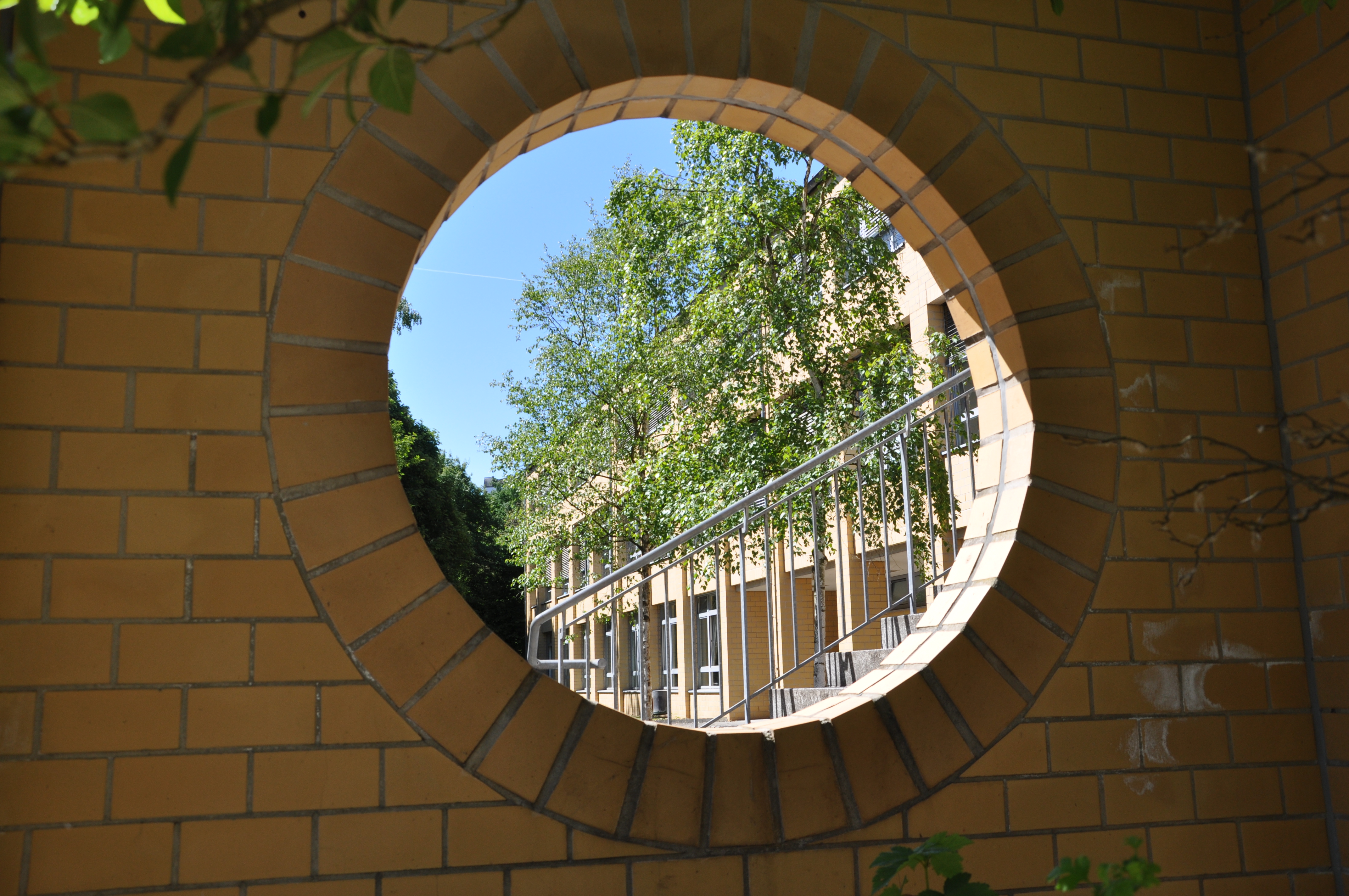 Blick auf das Schulgebäude Berufskolleg Eschweiler durch eine rund gemauerte Öffnung in der Wand