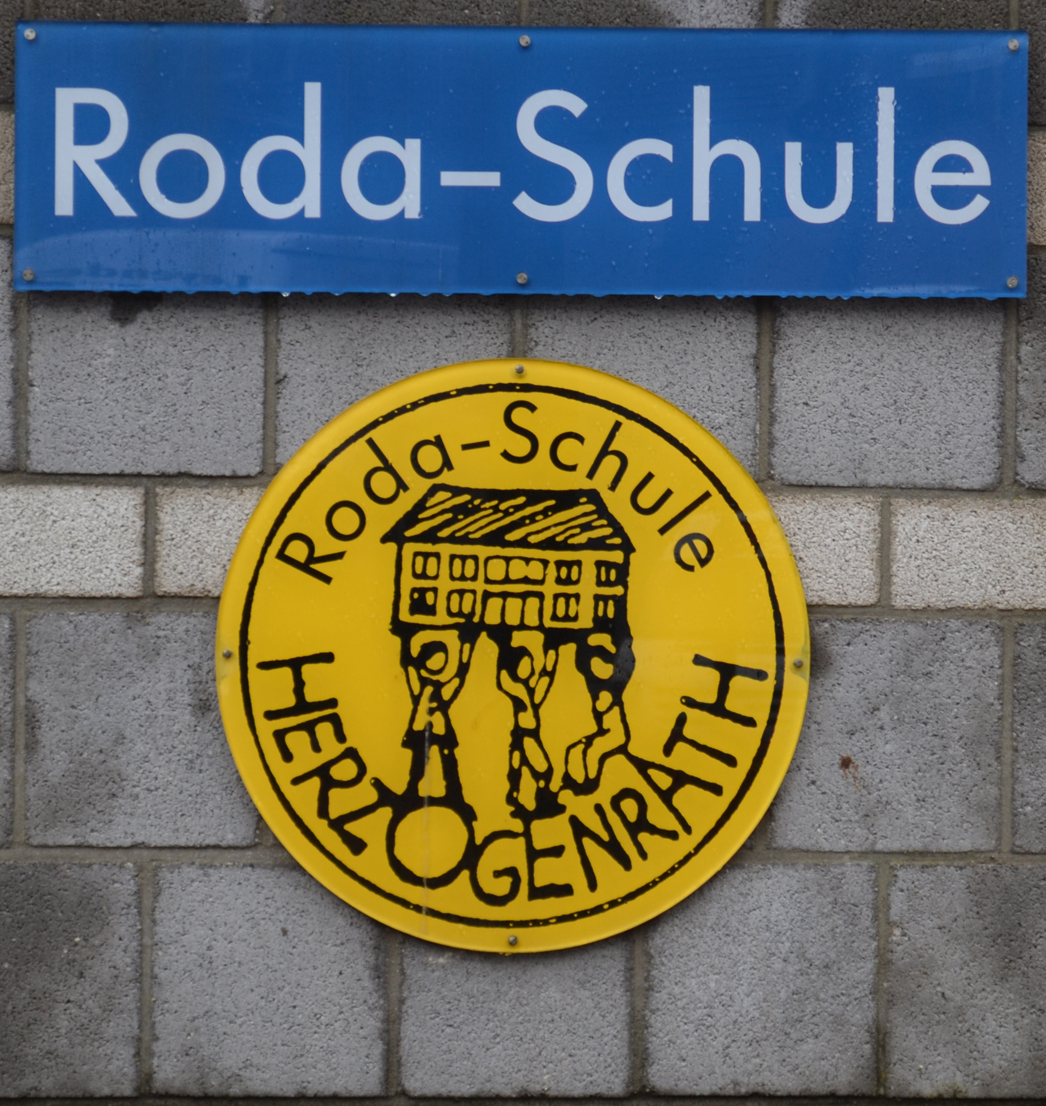 Schullogo an der Hauswand der Roda-Schule in Herzogenrath (Kinder, die eine Schule hochheben)