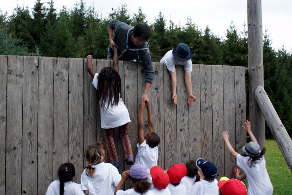 Kinder erklettern eine Holzwand und helfen sich gegenseitig