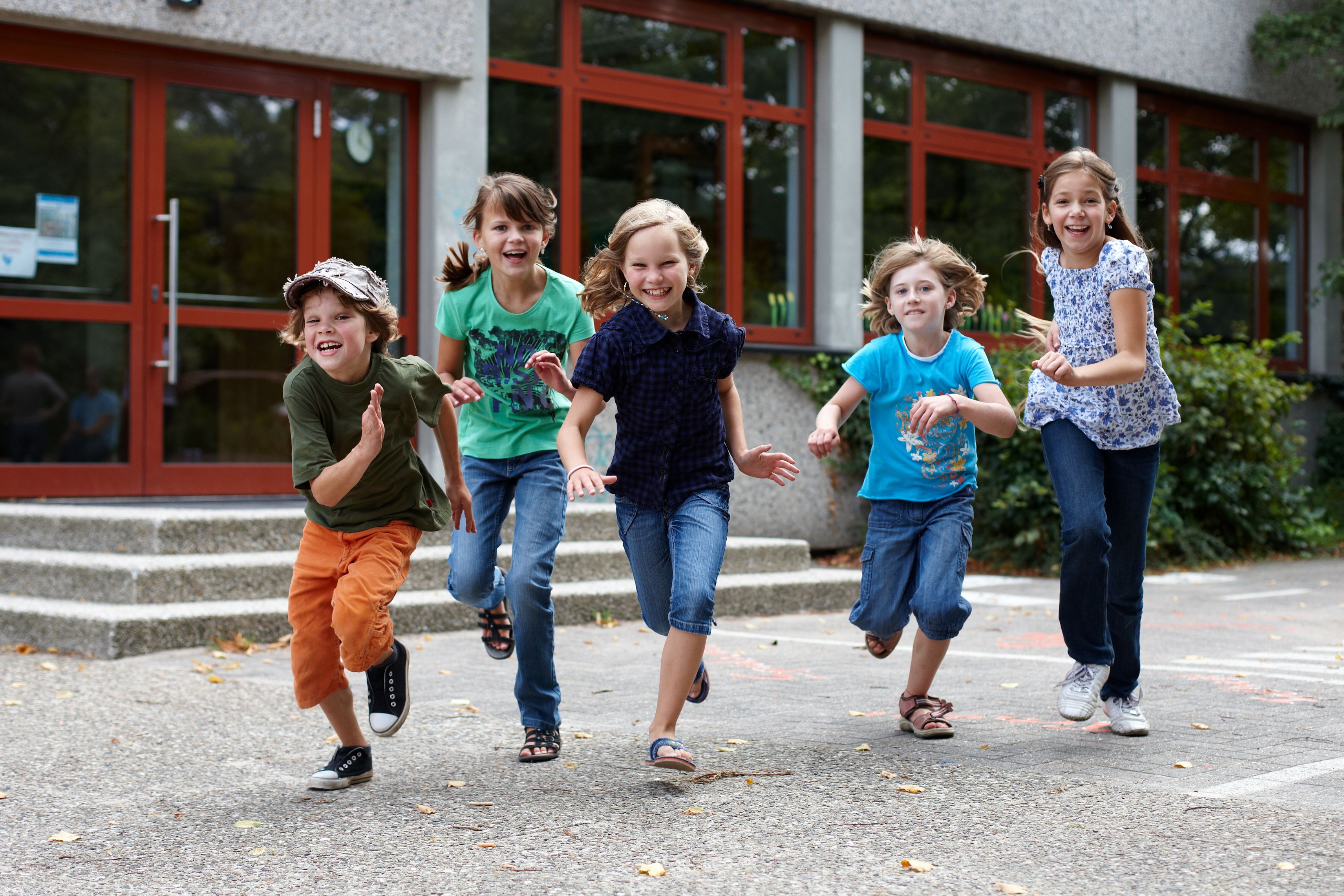 Fünf Kinder rennen über einen Schulhof und lachen