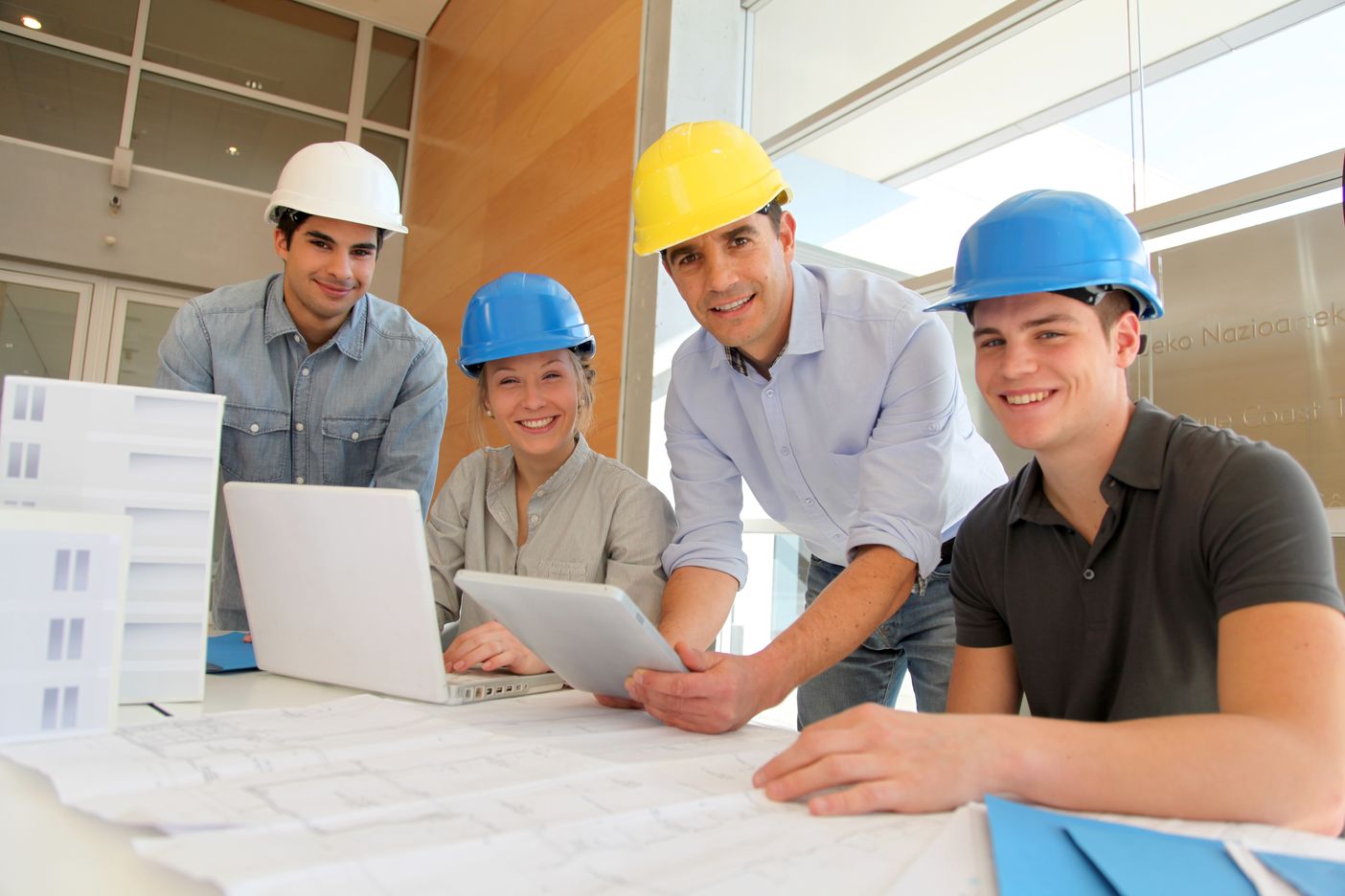 Drei Jugendliche und ein Erwachsener mit Bauhelmen in einem Bauingeniuerbüro