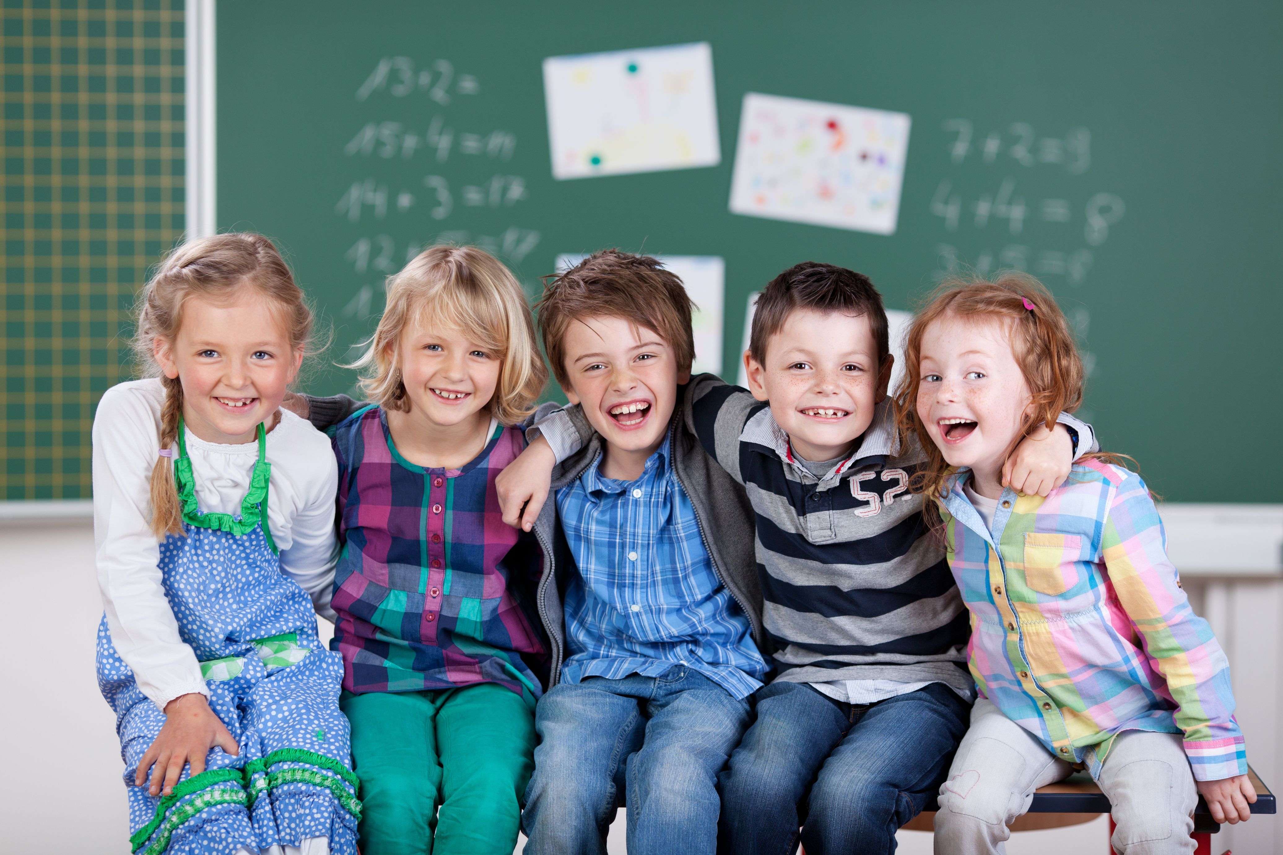 Fünf Grundschulkinder sitzen fröhlich vor einer Tafel 
