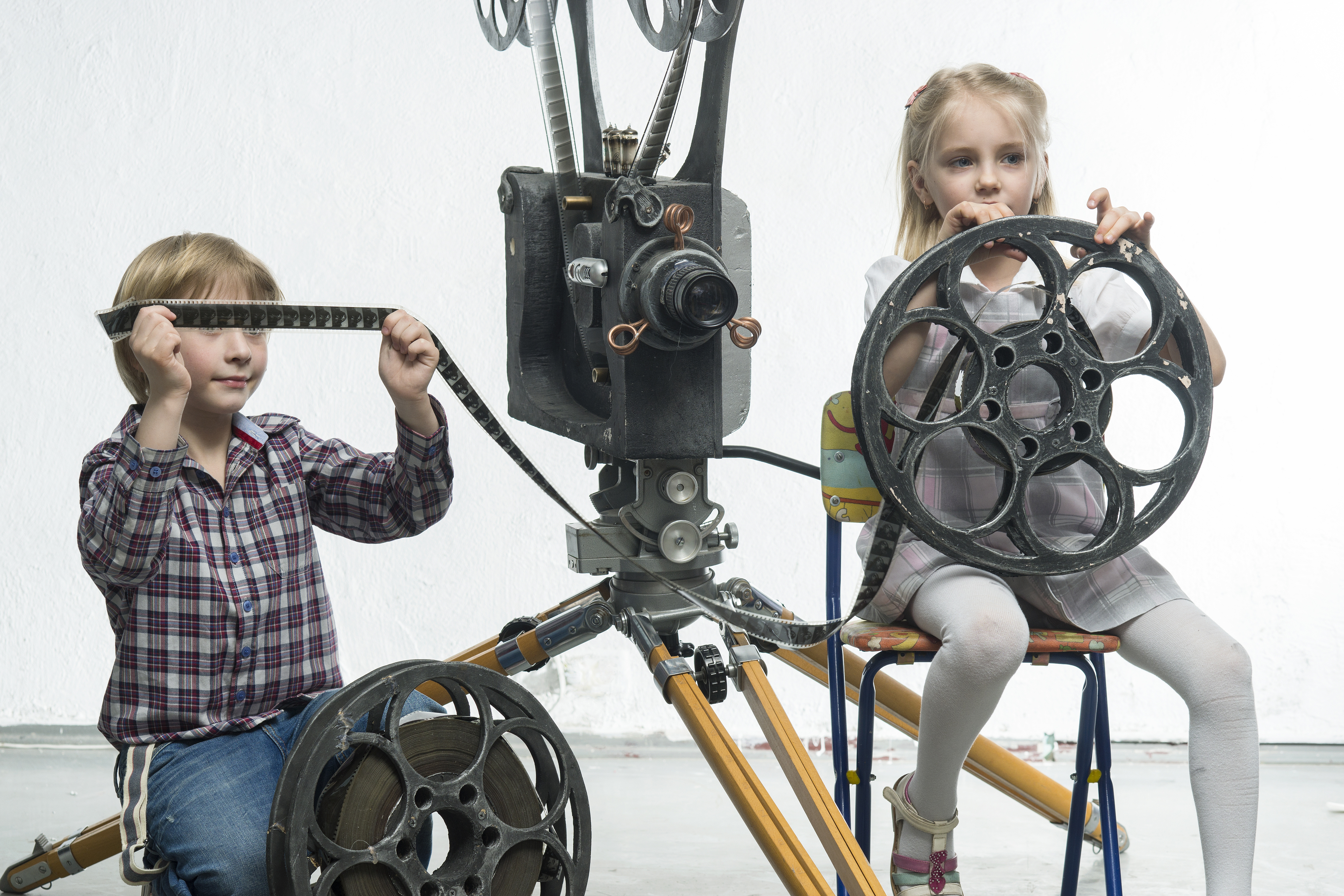 Junge und Mädchen spielen mit Filmrolle und Filmstreifen neben einem alten Filmprojektor