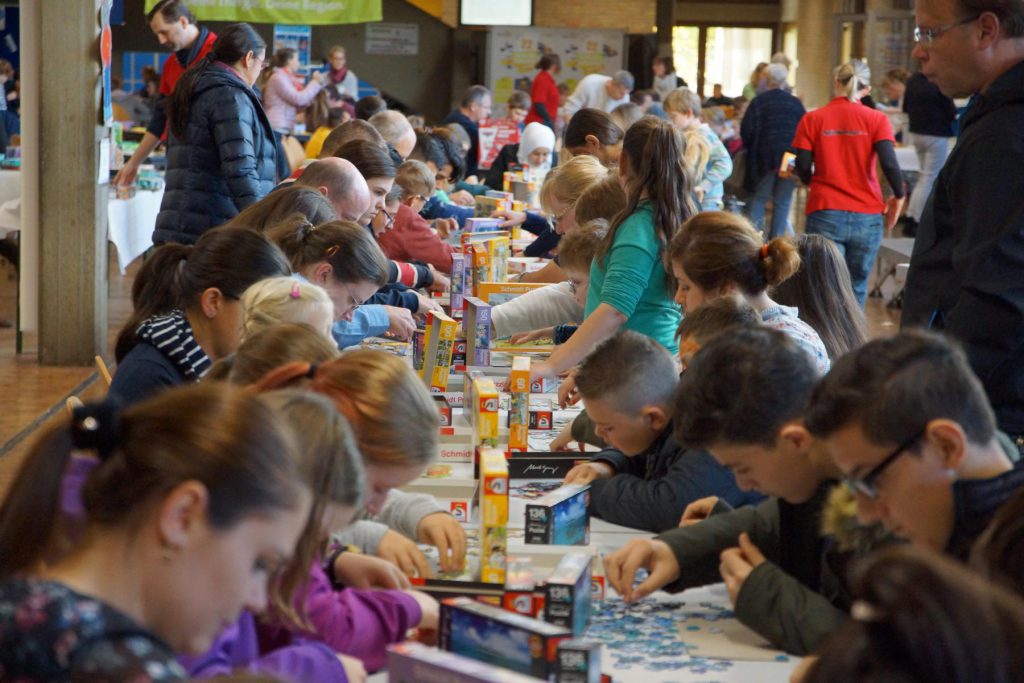 Kinder und Erwachsene legen Puzzle an einem langen Tisch