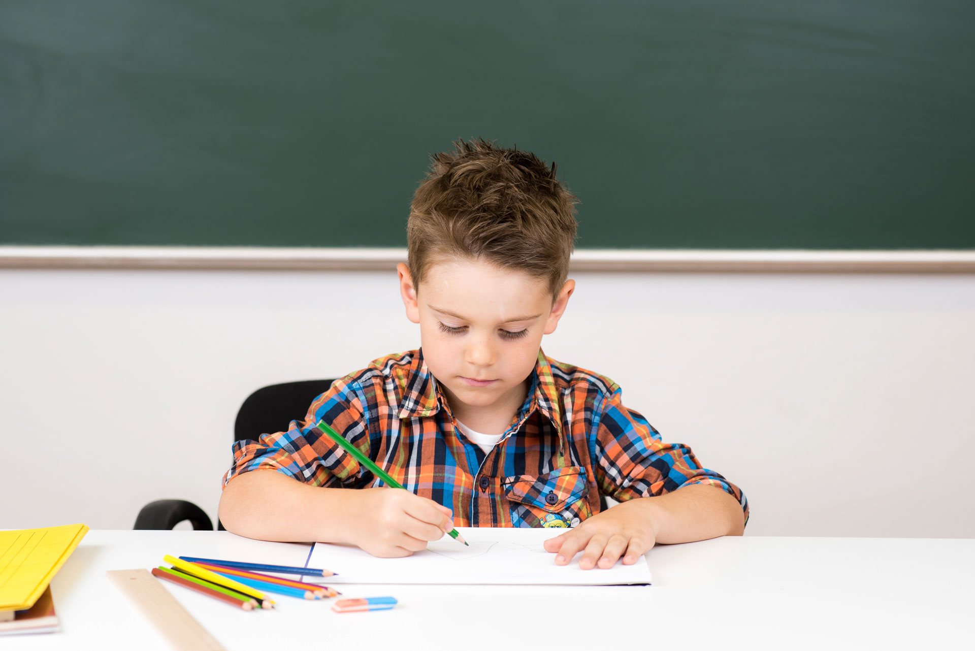 Ein Junge sitzt am Tisch und schreibt oder malt mit einem Stift auf Papier