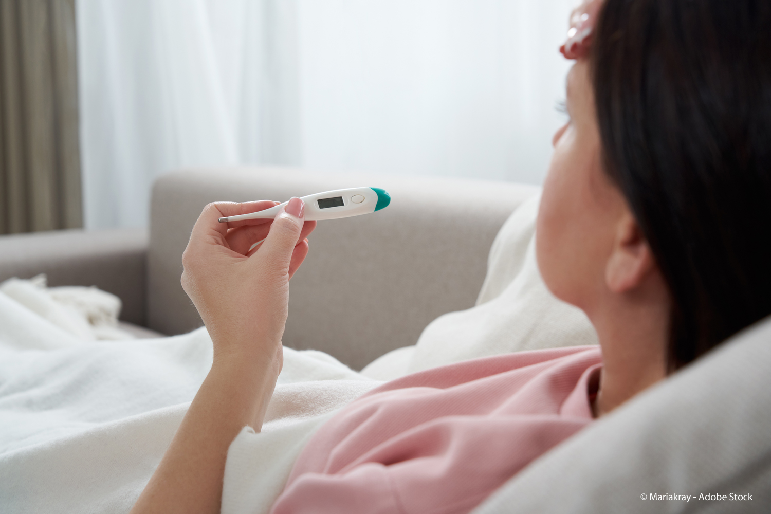 Frau liegt im Bett und hält ein Fieberthermometer